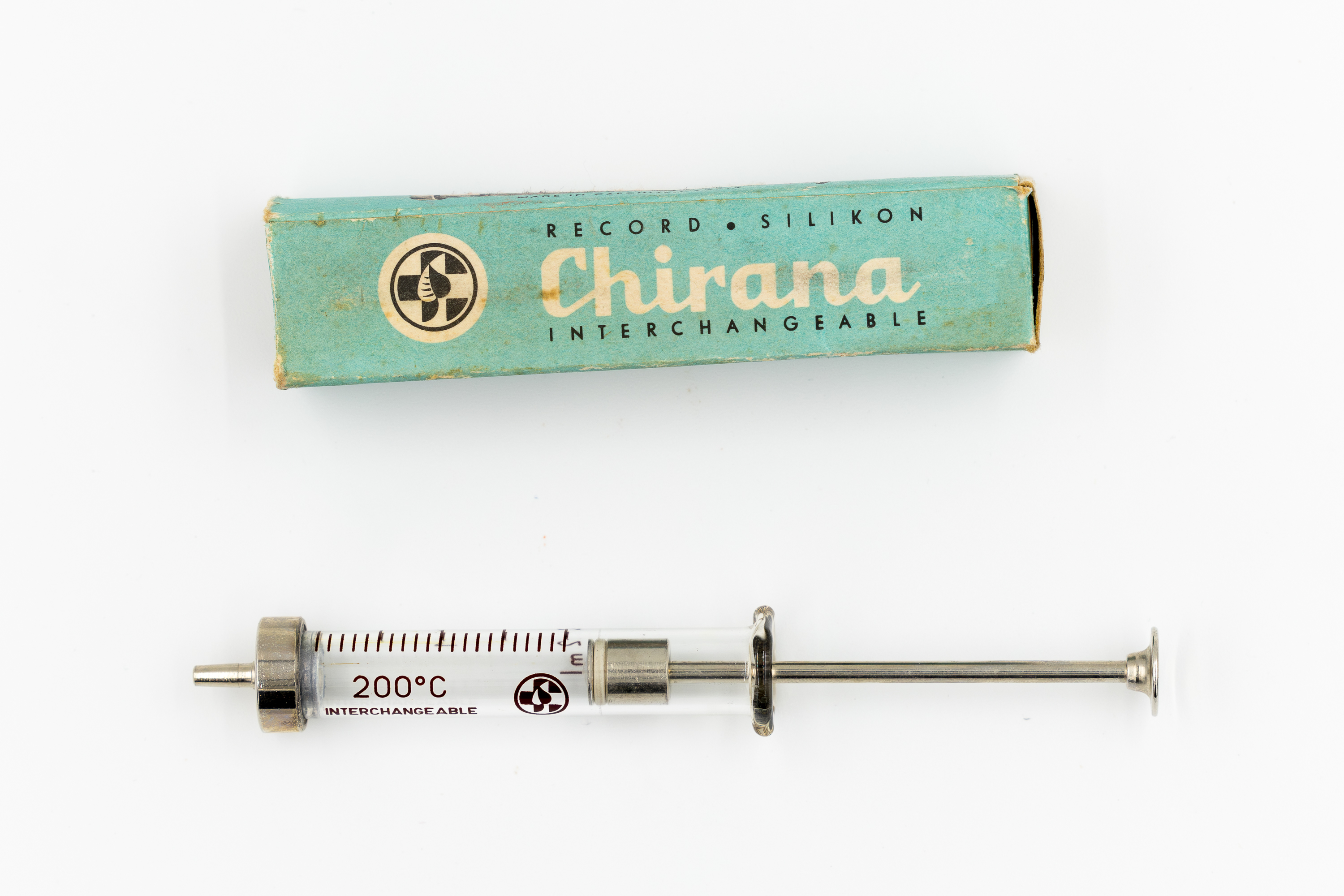 Na dole metalowo-szklana strzykawka, na górze pudełko tekturowe w kolorze seledynowym z napisem Record silicon chirana interchangeable