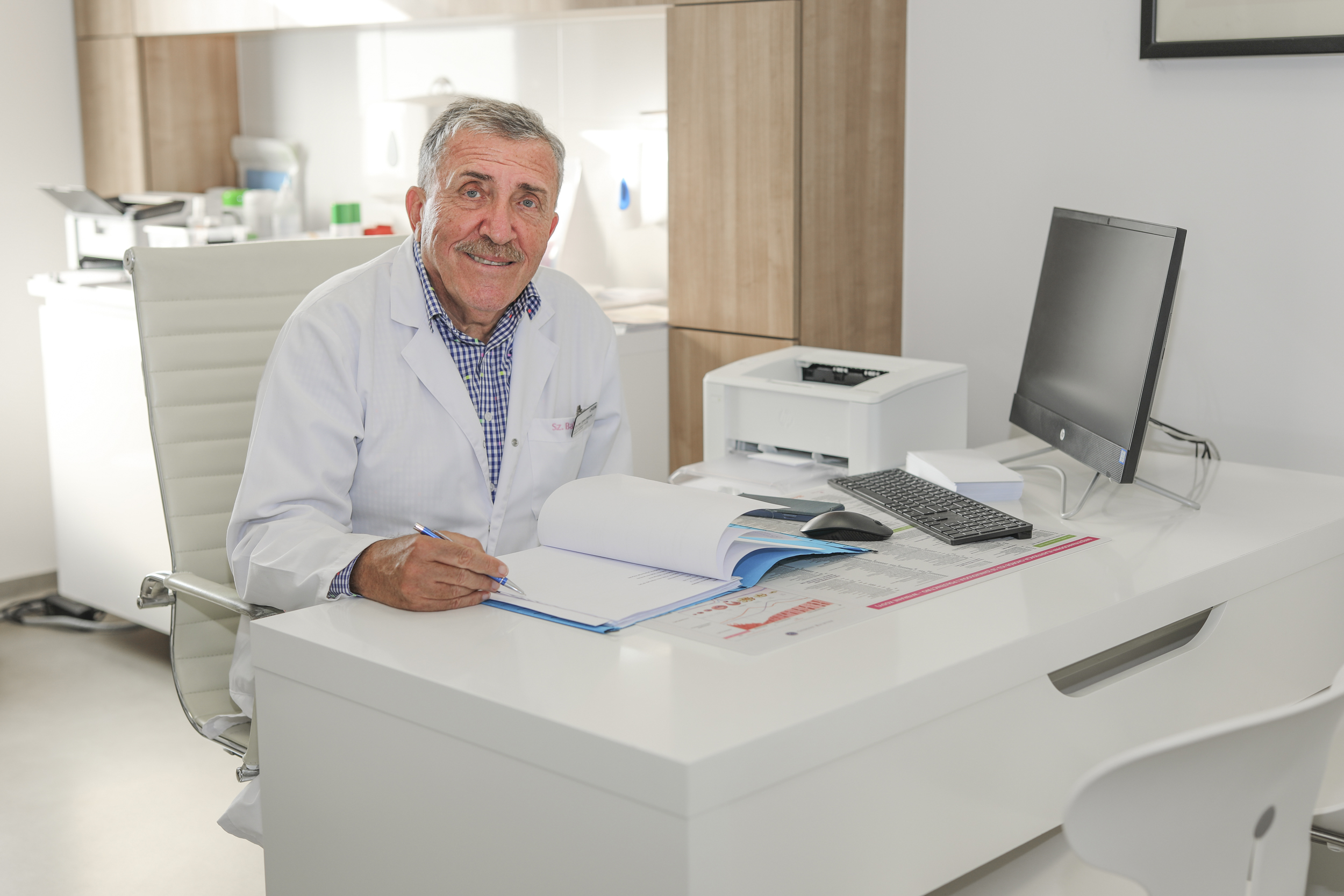 Uśmiechnięty pan siedzący przy biurku przed dokumentami i komputerem, trzymający w dłoni długopis