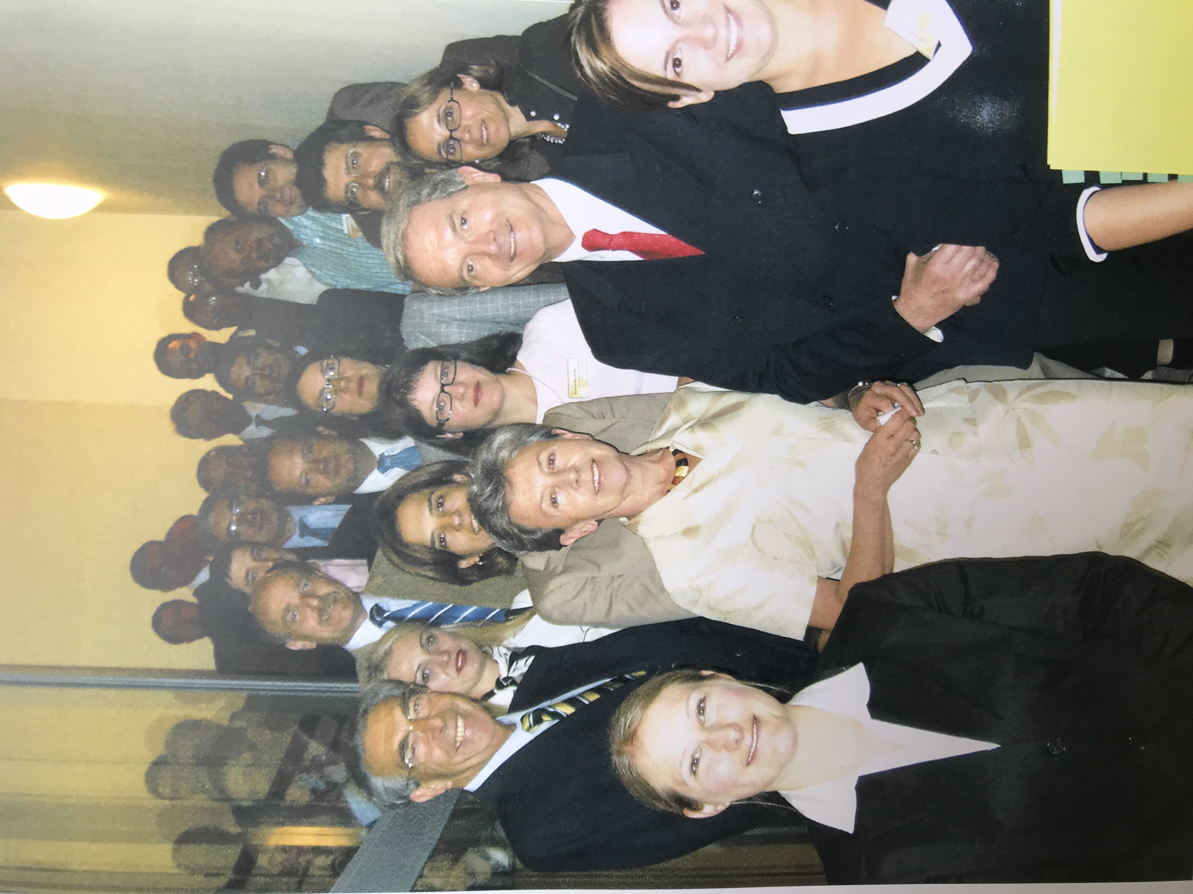 Duża grupa os&oacute;b elegancko ubranych, ustawionych na schodach w wąskim korytarzu.