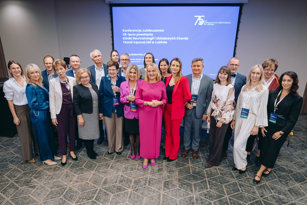 Bardzo wiele elegancko ubranych os&oacute;b patrzących przed siebie, uśmiechniętych, za nimi ekran.